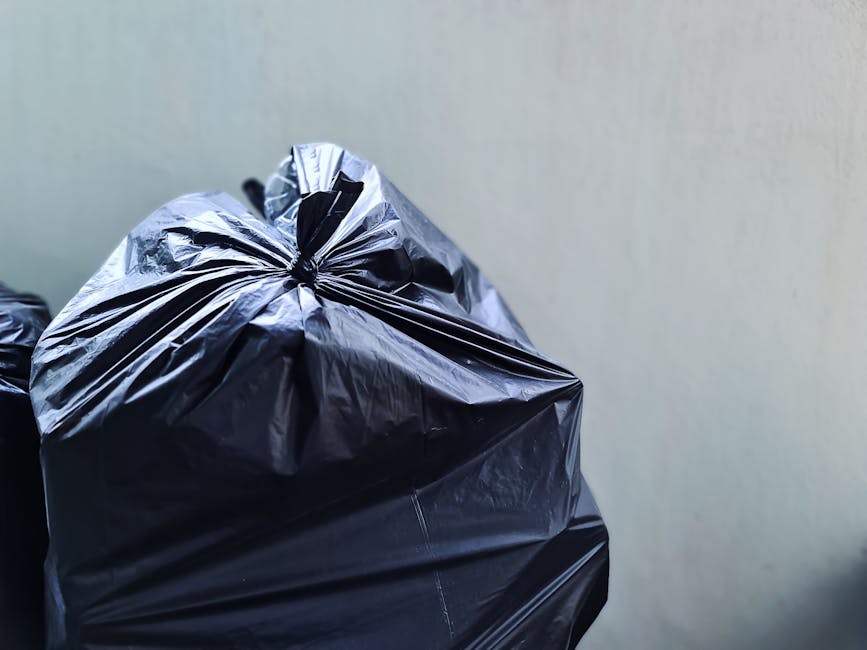 A close-up view of a pile of mixed waste materials scattered across a flat surface, including crumpled paper, plastic bottles, cardboard packaging, and foil wrappers. The paper debris appears worn and creased, with some torn edges, while the plastic bottles vary in shape and size, with labels partially visible and some caps still attached. Cardboard items are compressed and layered underneath other refuse, with a variety of textures from smooth to rough ridges. The background contains more scattered rubbish, with no clear organisation, creating a chaotic scene typical of waste accumulation for a private rubbish removal service. The lighting is diffuse, highlighting the different surfaces and textures of the rubbish, conveying a sense of disorder suitable for visual content about waste clearance or rubbish collection services. This scene offers an authentic snapshot of waste ready for disposal, compatible with a site specializing in alternative rubbish removal methods, such as on-site clearance or private disposal options.
